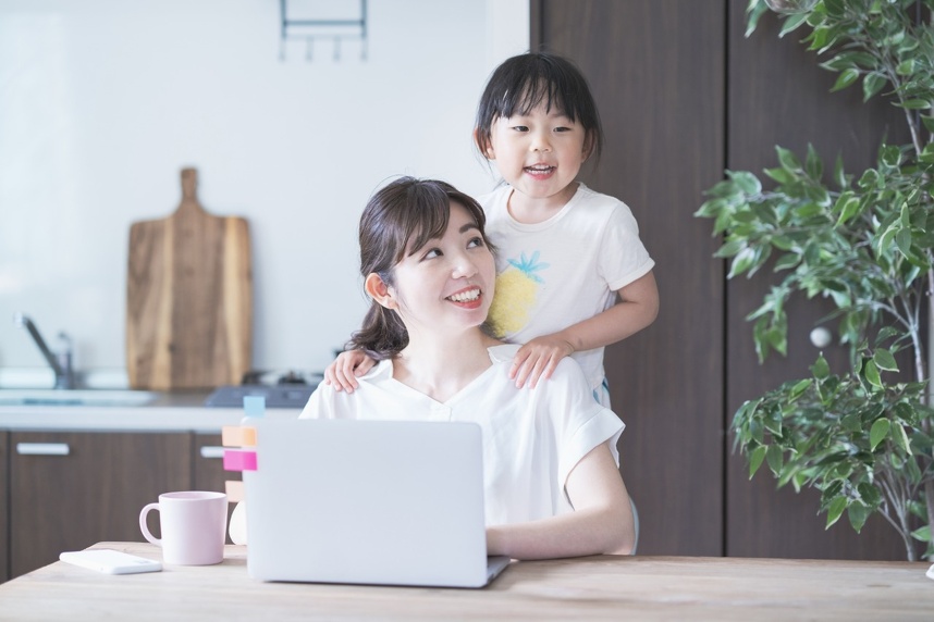 家で子どもと遊びながらパソコンを操作する女性