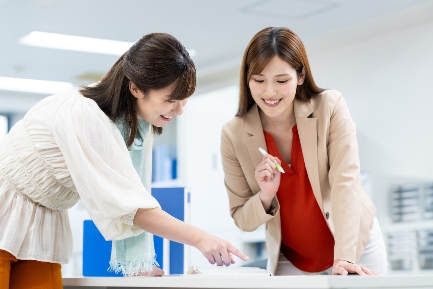 オフィスにて机にある紙を見てやりとりしている女性二人